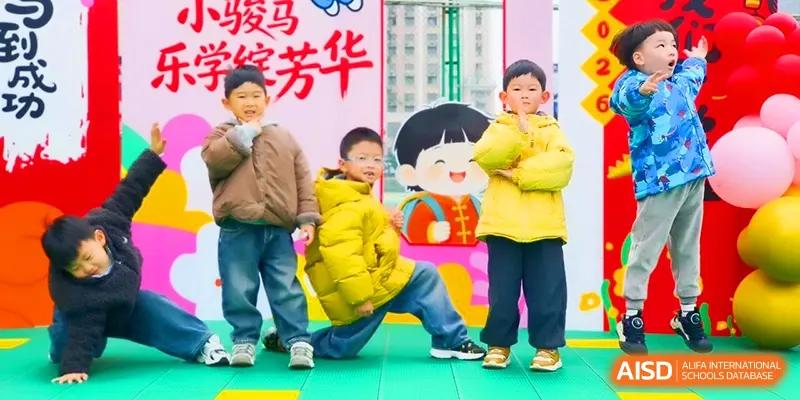 Three young students in warm winter jackets pose playfully in front of a colorful cartoon backdrop at Walton-Hefei School.
