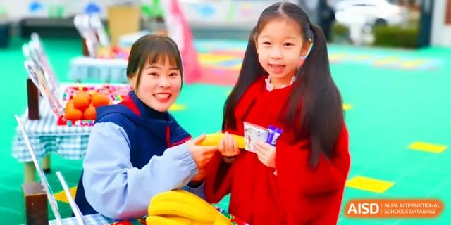 A smiling teacher hands a healthy banana snack to a young student during a break between classes at Walton-Hefei School.