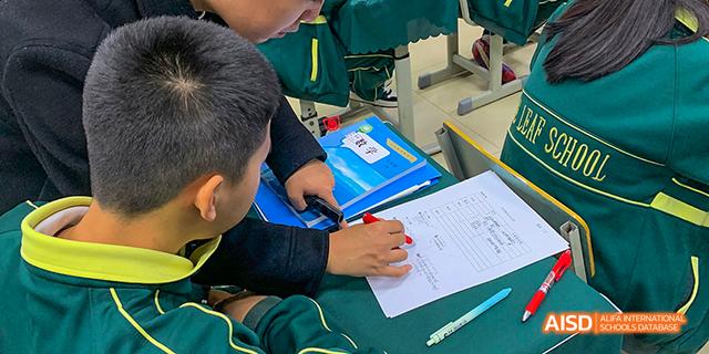 A close-up of a student's hands working on a worksheet and using a calculator during a class at Maple Leaf International School Chongqing.