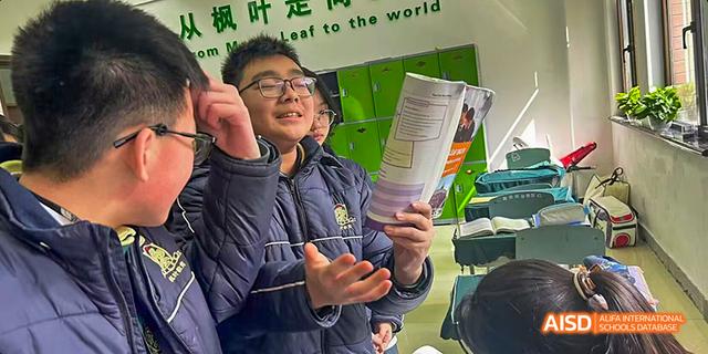 A smiling male student holding up a textbook and looking engaged during a classroom discussion at Maple Leaf International School Chongqing.
