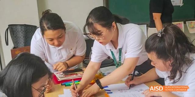 A female teacher with glasses kneeling down and assisting a student with their schoolwork at Maple Leaf International School Chongqing.