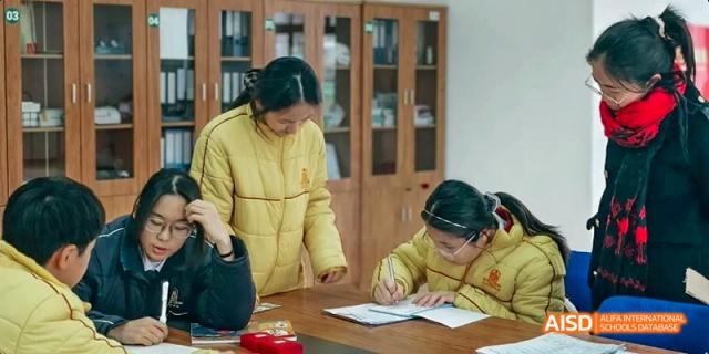 A female teacher assisting a young student with writing or schoolwork in an indoor setting at Maple Leaf International School Chongqing.