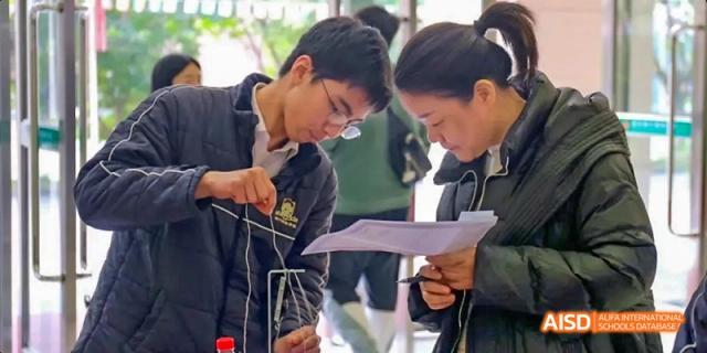 Two students working together on a hands-on physics or science experiment while reviewing a worksheet at Maple Leaf International School Chongqing.