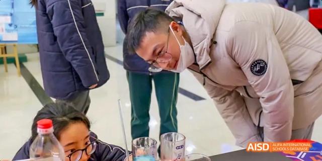 A male student wearing safety goggles bending over a science experiment with glassware on a table at Maple Leaf International School Chongqing.