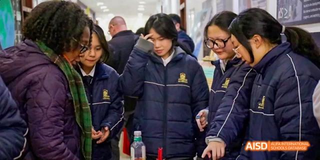 A female student in a uniform jacket participating in an indoor science demonstration or activity at Maple Leaf International School Chongqing.