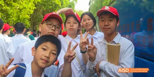 A close-up of a group of happy students outdoors, some wearing red caps and making peace signs with their hands, at Maple Leaf International School Chongqing.