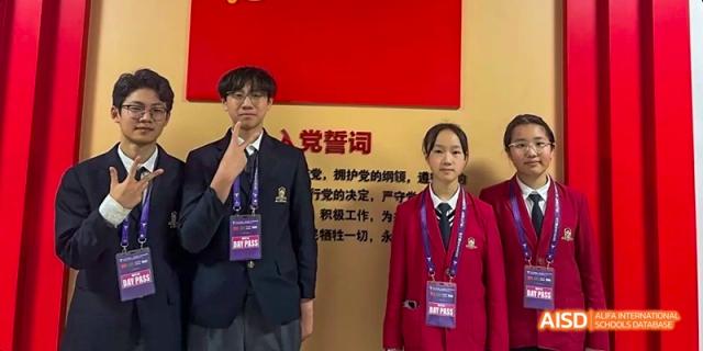 Two students in school uniforms (a male in black and a female in red) standing in front of a red wall with Chinese text at Maple Leaf International School Chongqing.