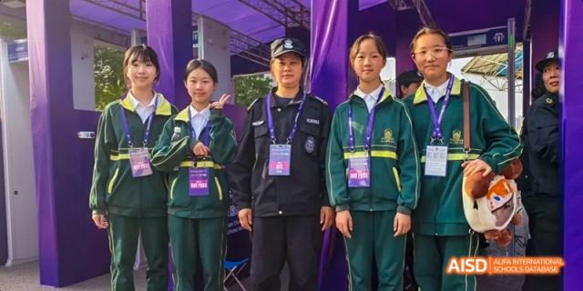 Two smiling female students in school uniforms posing with an adult wearing a security or official's uniform at an event at Maple Leaf International School Chongqing.