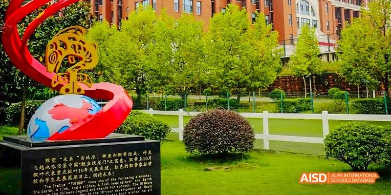 A well-maintained outdoor area with green trees, grass, a white fence, and a rounded hedge, likely part of the campus grounds at Maple Leaf International School Chongqing.