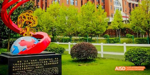 A well-maintained outdoor area with green trees, grass, a white fence, and a rounded hedge, likely part of the campus grounds at Maple Leaf International School Chongqing.