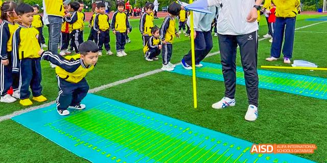 Students in yellow and black uniforms participating in an outdoor activity or sports day event on a green field with blue markings at Maple Leaf International School Chongqing.