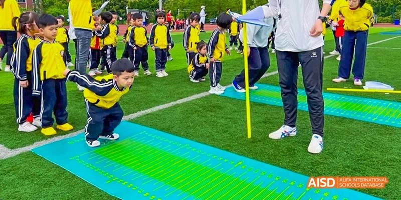 A close-up view of students in uniform lined up on a green and blue marked sports field, with an adult's legs visible, at Maple Leaf International School Chongqing.