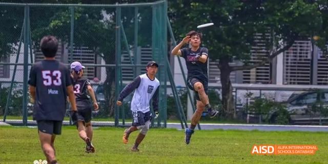 Two young men playing Ultimate Frisbee, with one jumping high to catch the disc, as part of a sports program at Maple Leaf International School Chongqing.