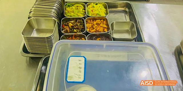 A tray of cooked food, including stir-fried vegetables and meat dishes, ready for serving in the cafeteria at Maple Leaf International School Chongqing.