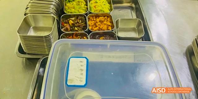 A tray of cooked food, including stir-fried vegetables and meat dishes, ready for serving in the cafeteria at Maple Leaf International School Chongqing.