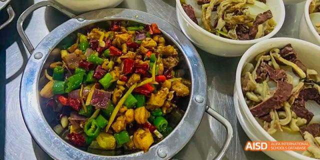 A dish of spicy stir-fried chicken with chili peppers and diced vegetables, likely served in the cafeteria at Maple Leaf International School Chongqing.