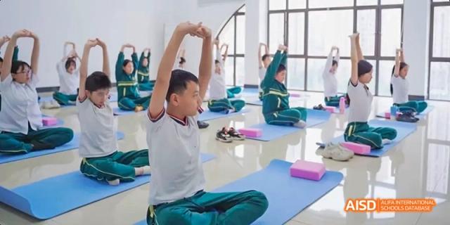 Students wearing green and white practicing yoga or a stretching exercise on mats in a classroom or gym at Maple Leaf International School Chongqing.