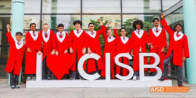Canadian International School of Beijing graduates in red robes standing behind large white letters that spell "CISB.