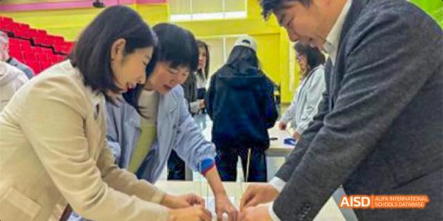 Canadian International School of Beijing students and an instructor working together on a project, with a focus on their hands writing and drawing on a table.