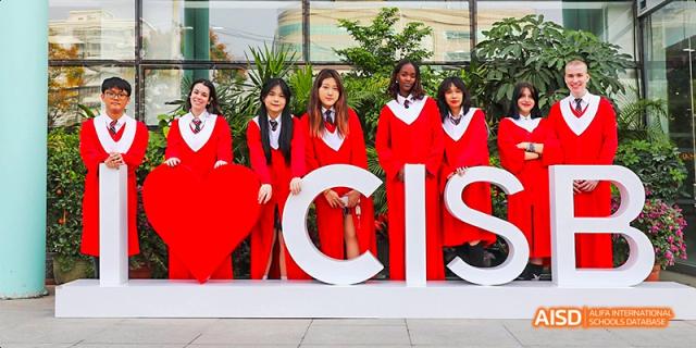 Canadian International School of Beijing graduates in red robes standing behind large white letters that spell "CIS.