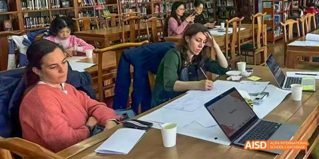 Canadian International School of Beijing students working individually with laptops and papers at wooden desks in a library or study area.