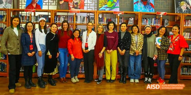 A group of Canadian International School of Beijing students and teachers posing for a group photo in a library, standing in front of bookshelves.