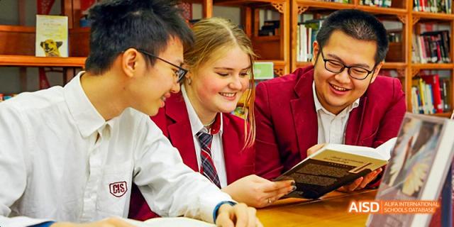 Canadian International School of Beijing students smiling and reading a book together at a table.