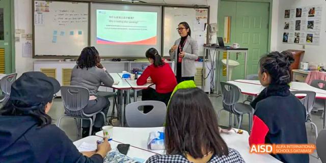 A Canadian International School of Beijing teacher giving a presentation to students in a classroom with a large screen.