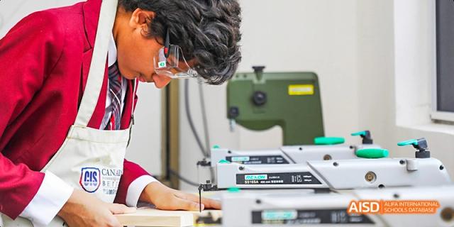 A Canadian International School of Beijing student in a red uniform working on a woodworking or art project.