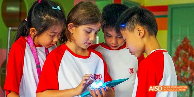 A close-up of Canadian International School of Beijing students in red and white uniforms looking at a digital tablet together.