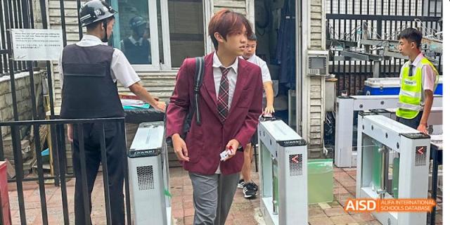 A Canadian International School of Beijing student in a red uniform walking through a gate at the school entrance.
