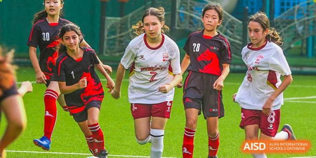 Canadian International School of Beijing students in soccer uniforms running on a field during a game.