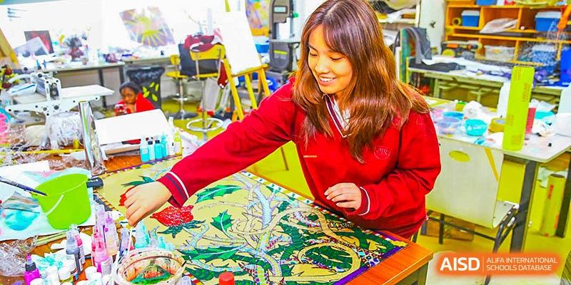 Canadian International School of Beijing female student in a red sweater working on a large, colorful art project or puzzle in a classroom.