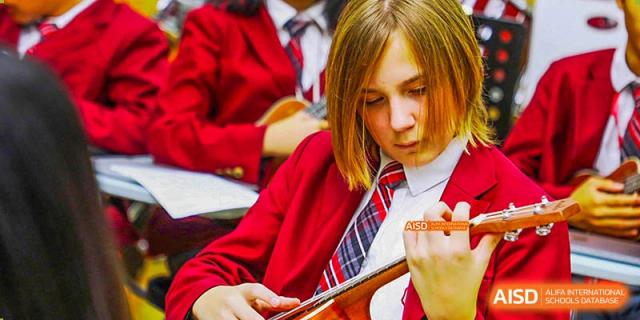 Canadian International School of Beijing female student in a red uniform playing a stringed instrument in a classroom.