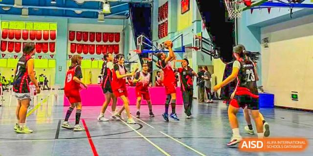Canadian International School of Beijing students play basketball during a game in a gymnasium.