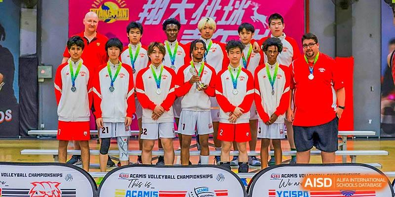 A Canadian International School of Beijing sports team, wearing red and white tracksuits with medals, poses together after a competition.