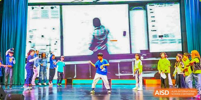 Canadian International School of Beijing students perform a dance on a stage in front of a large digital screen.