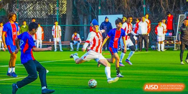A Canadian International School of Beijing soccer player, wearing a red and blue striped jersey, kicks the ball during a game.