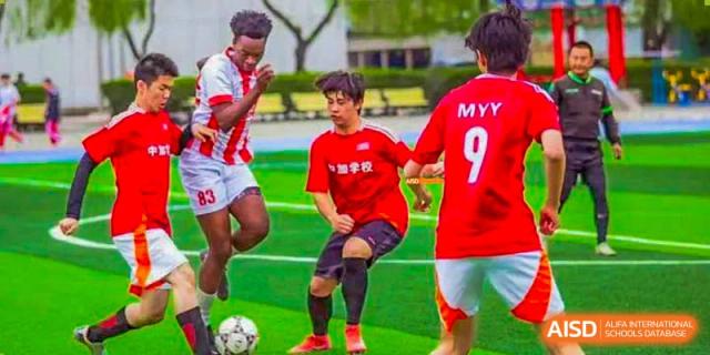 Canadian International School of Beijing male students in red and white jerseys playing soccer on a field.