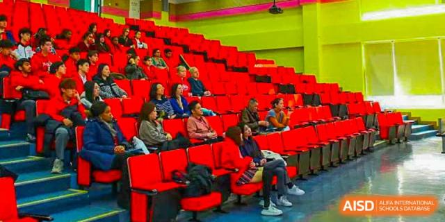 An audience watches a Canadian International School of Beijing performance or sports game from red stadium seating.