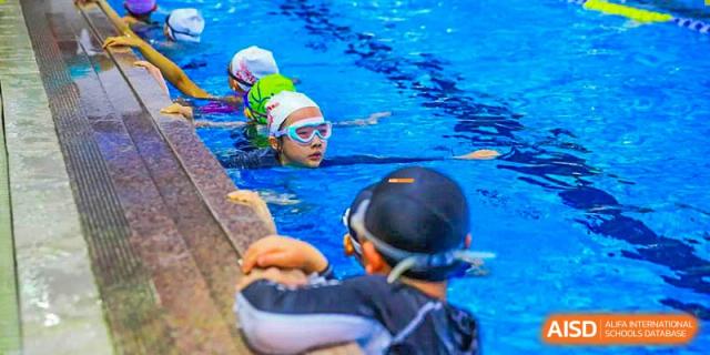 A Canadian International School of Beijing student in a green swim cap and goggles learns to swim with an instructor.