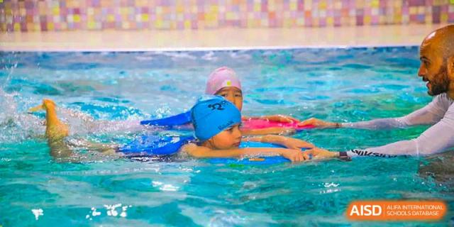 Two Canadian International School of Beijing students practice swimming in a pool, one floating on their back while the other assists them.