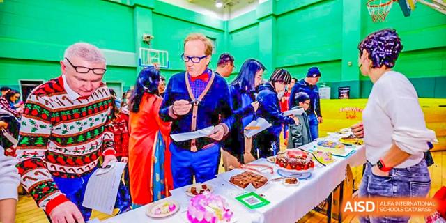 A Canadian International School of Beijing staff member with a medal stands behind a table full of food and desserts.