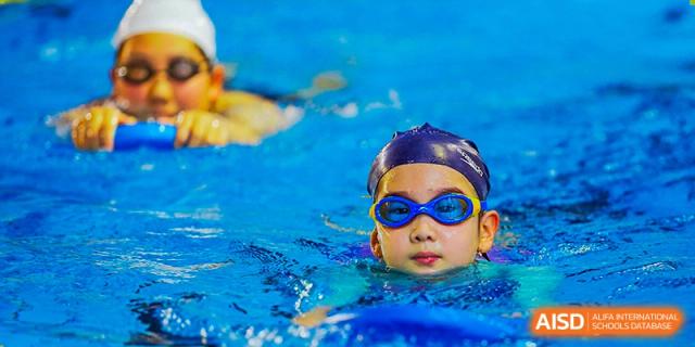A Canadian International School of Beijing student in a black swim cap and goggles is in a swimming pool, looking at the camera.