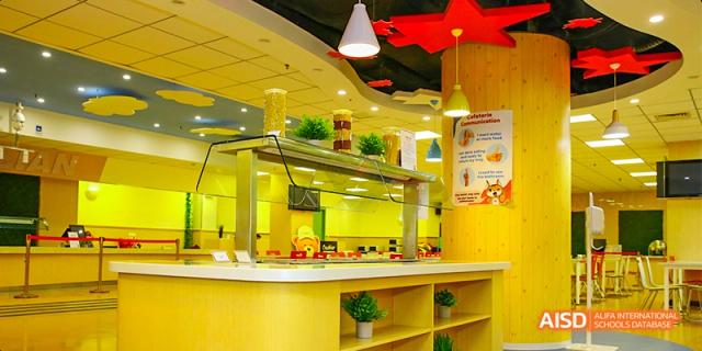 The bright and modern cafeteria at the Canadian International School of Beijing, with a food service counter and yellow-themed decor.