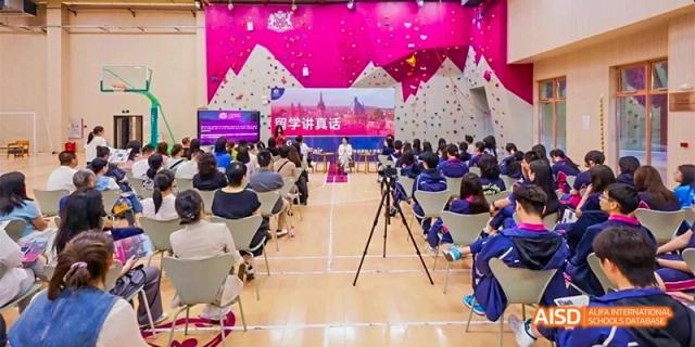 Students and adults attending a lecture or presentation in a large, brightly decorated hall with pink walls at Fettes College Guangzhou.
