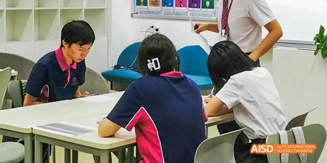 A student at Fettes College Guangzhou sitting at a desk and facing a whiteboard with a colorful array of charts or class notices.