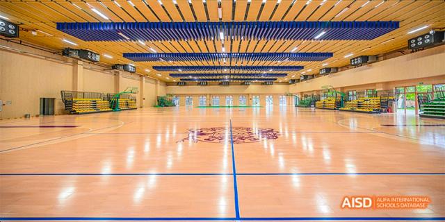 The large, bright indoor gymnasium court at Fettes College Guangzhou, featuring a polished wooden floor with blue markings and high ceilings.