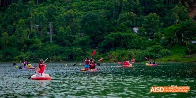Two people from Fettes College Guangzhou paddling a canoe or kayak on a lake surrounded by dense green forest during an outdoor activity.