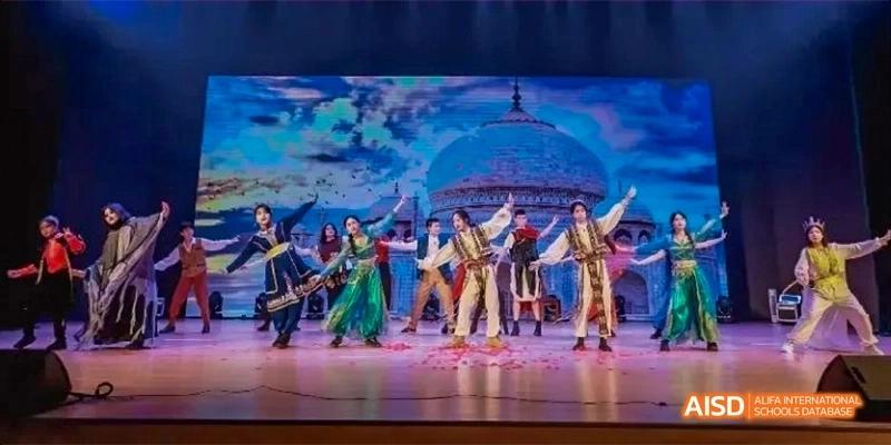 Students from Fettes College Guangzhou performing a colorful cultural or dramatic dance on a stage with a scenic, dome-shaped backdrop.